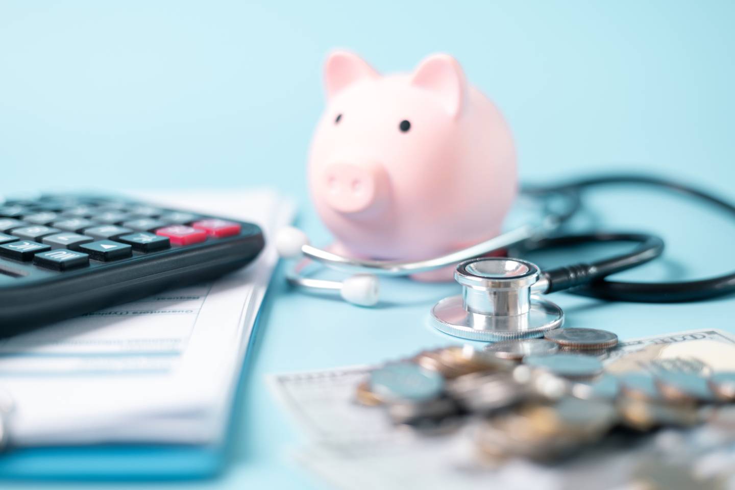 A blue background with a piggybank and stethoscope placed next to some paperwork