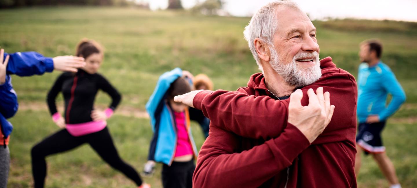 an active mature man stretching in a park with members of a running group