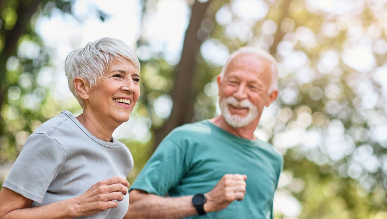 mature couple running and smiling through the park