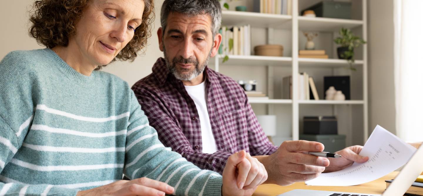 Mature couple concentrating on calculating household expenses with a laptop and papers