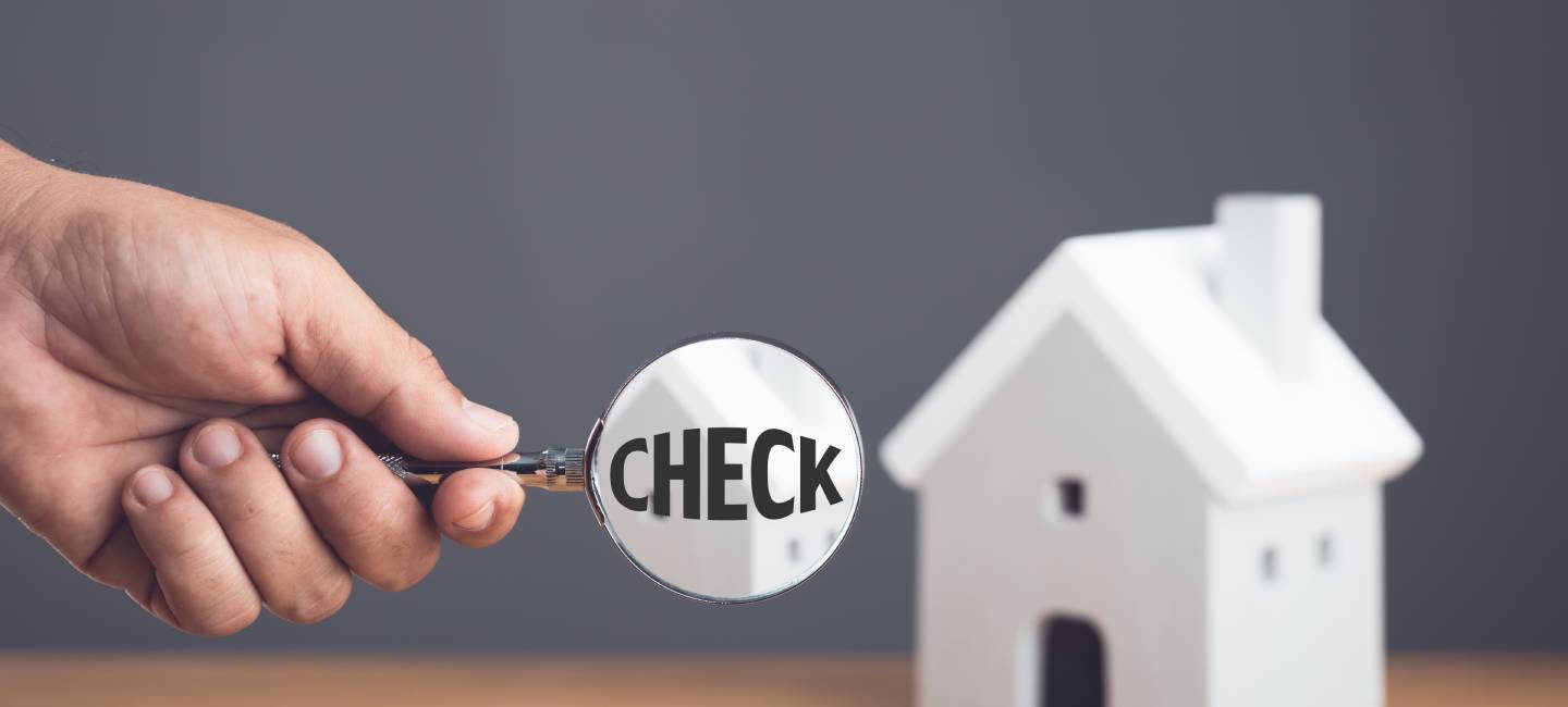 Hand holding a magnifying glass and inspecting the house model on wooden desk. 