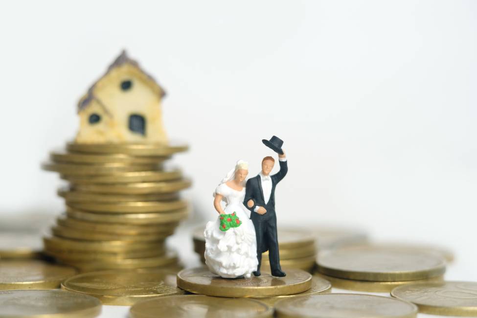 Bride and groom standing above coin pile in front of mini house isolated on white background. Image photo