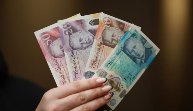 A person is holding four new bank notes with King Charles' face on it - a £50, £20, £10 and a £5 note