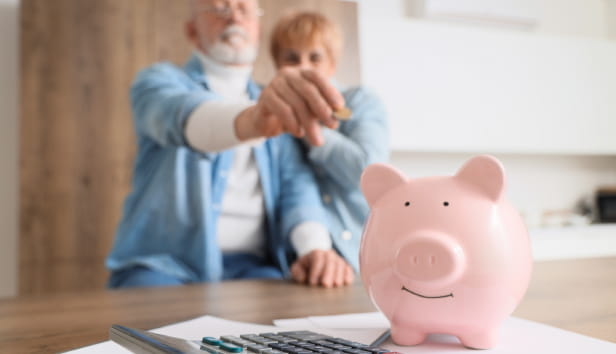 Mature couple putting coin into piggy bank in kitchen, closeup