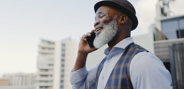 A man with a hat and beard talking outdoors, laughing and chatting on his mobile phone