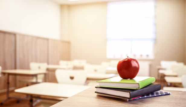 School teacher's desk with stack of books and apple.