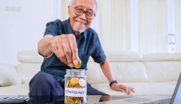 Happy senior man savings golden coins in a jar with retirement text and laptop on the table