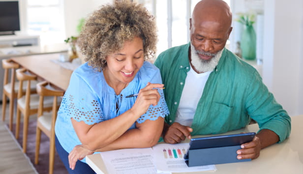 Smiling Mature Couple At Home With Digital Tablet Looking At Domestic Finances