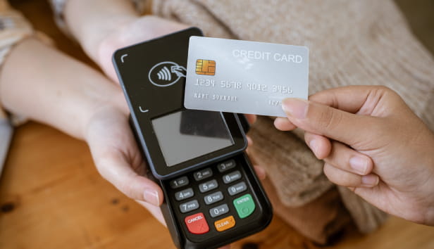 A close-up image of a customer tapping her credit card with a payment terminal or credit card machine at a cashier in a clothing store. cashless payment, card reader, electronic funds transfer