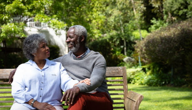 Front view of senior African American couple in the garden, sitting on a bench, embracing and talking. Family enjoying time at home, lifestyle concept.
