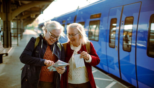 Two senior women at train station with map.