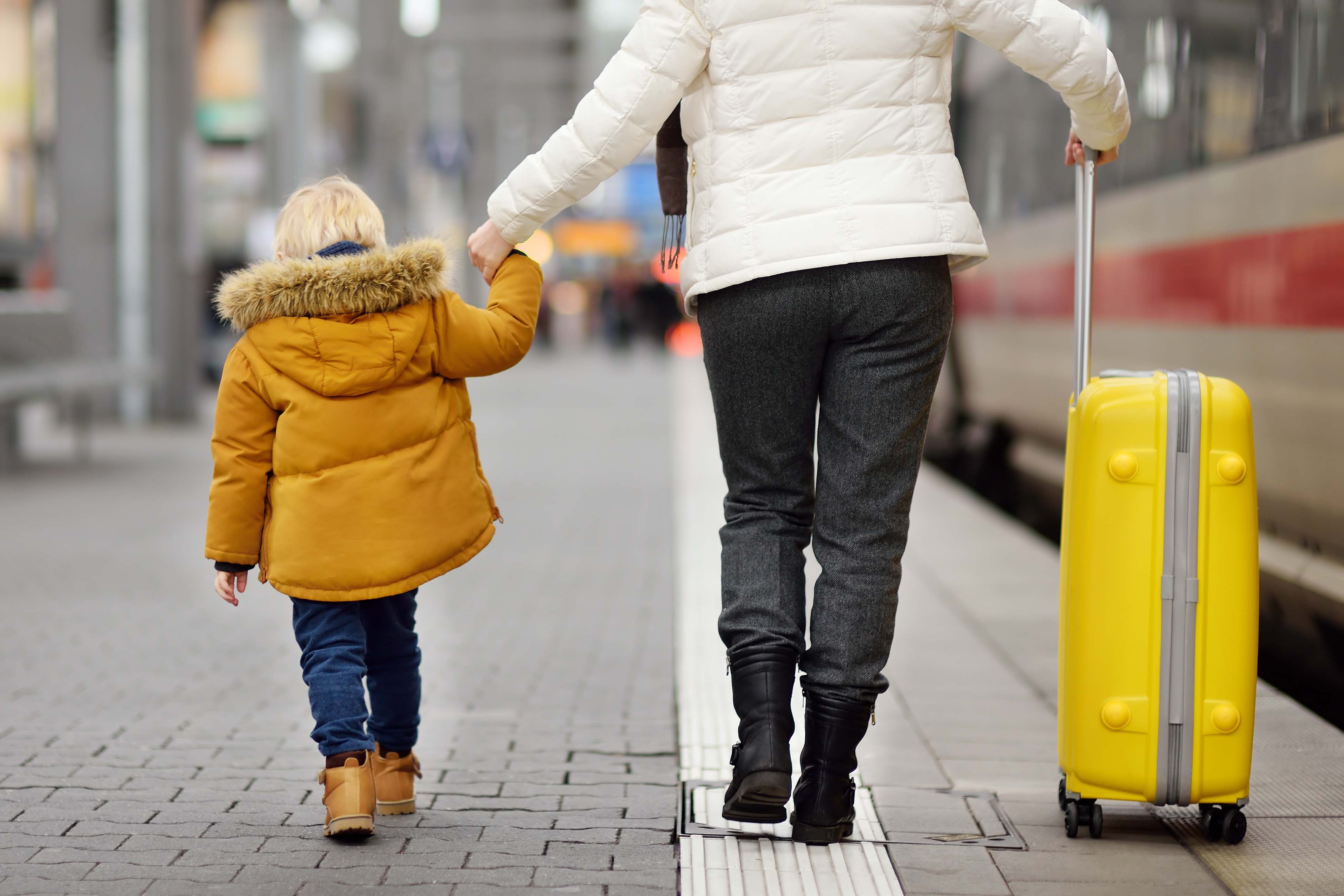 Woman holding her son's hand and a suitcase on a train station platform