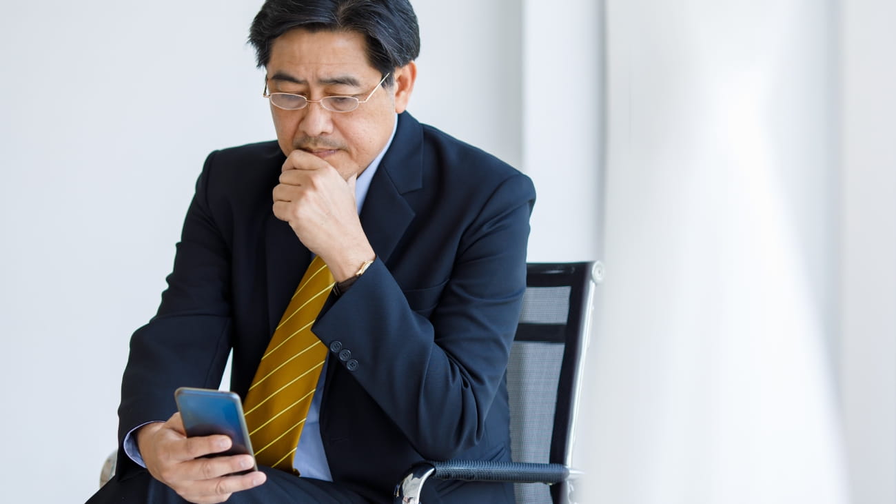 A man sat on a chair in a suit using a mobile phone