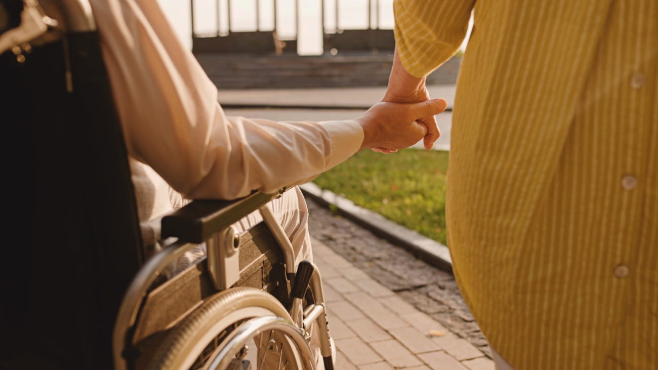 Two people holding hands - one is sat in a wheelchair and one is stood up