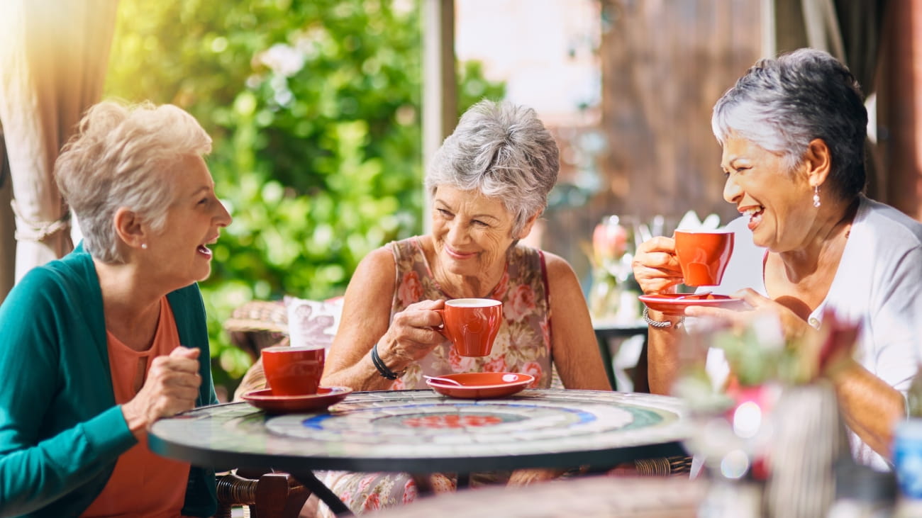 Three ladies laughing and drinking cups of coffee