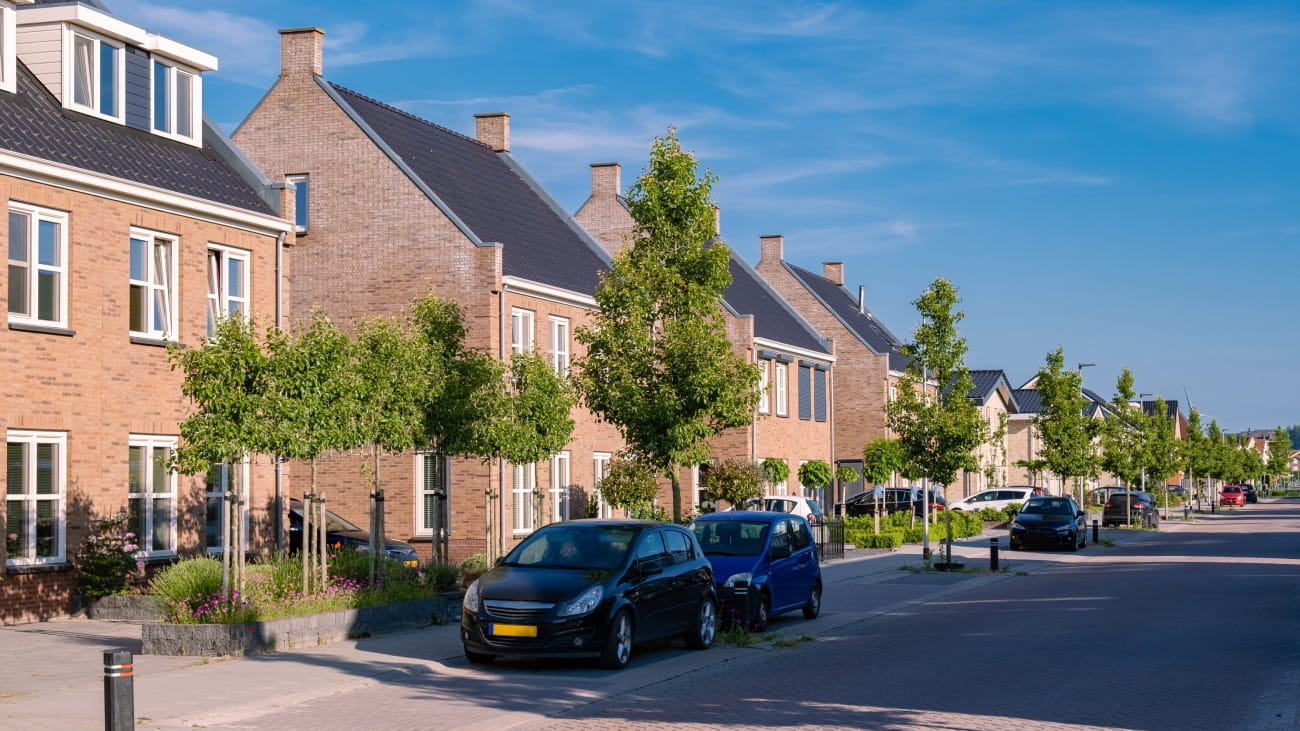 A row of houses on a lovely looking street. There are two cars parked outside.
