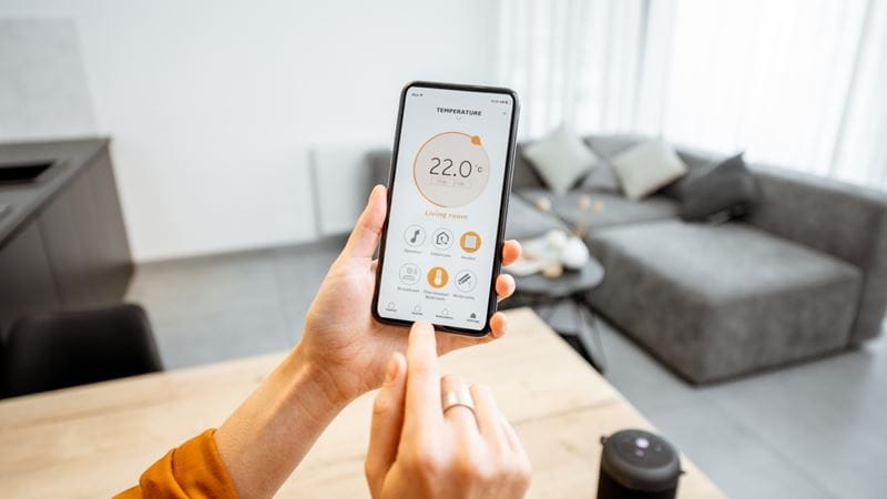 A person is using an app on their smartphone to control the temperature of their house from 