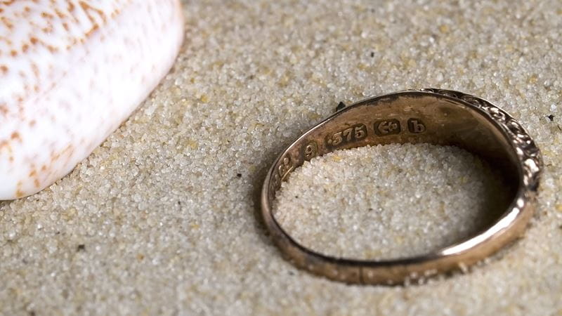 A 9ct gold ring on the beach with hallmark clearly displayed.