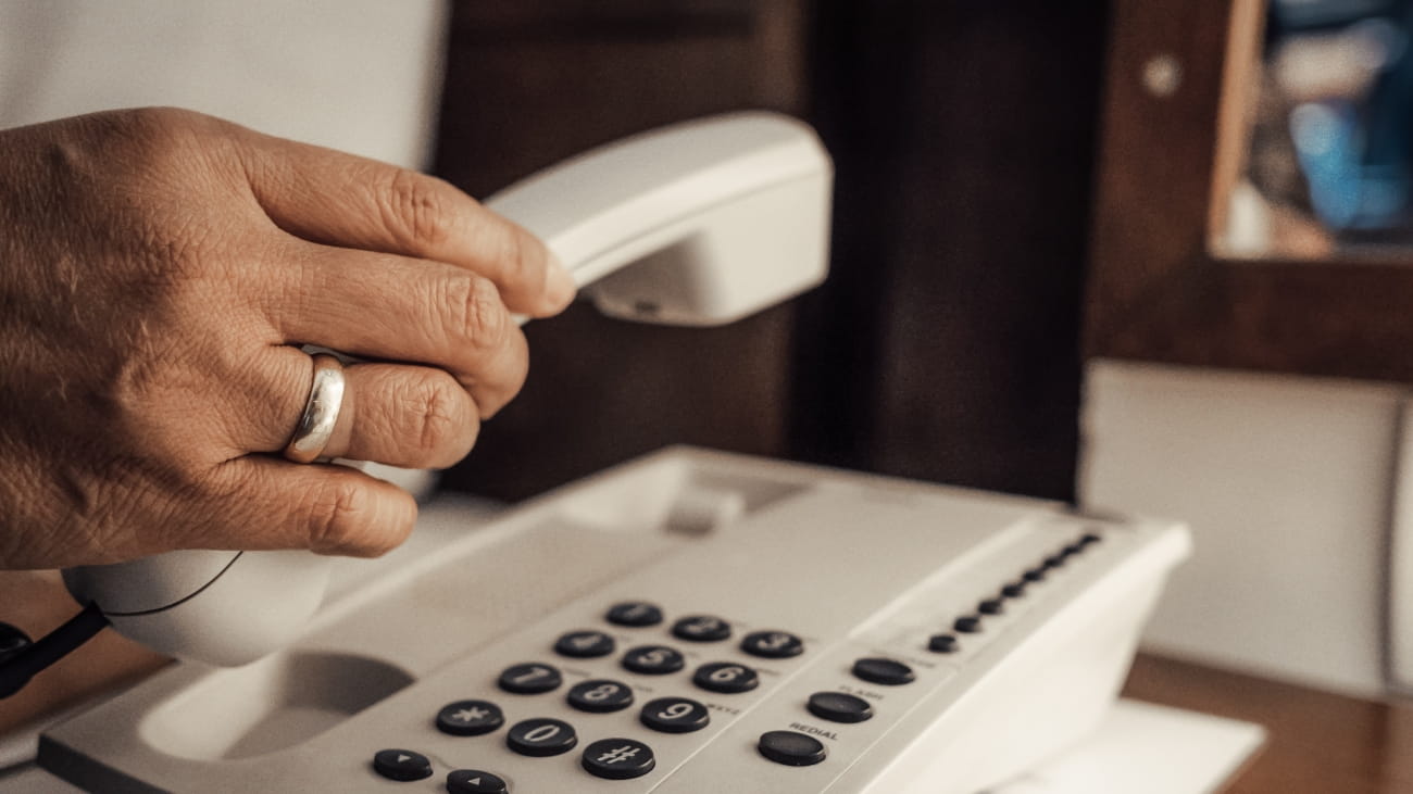 Closeup of female hand holding telephone receiver and dialing a phone on a classical white telephone.