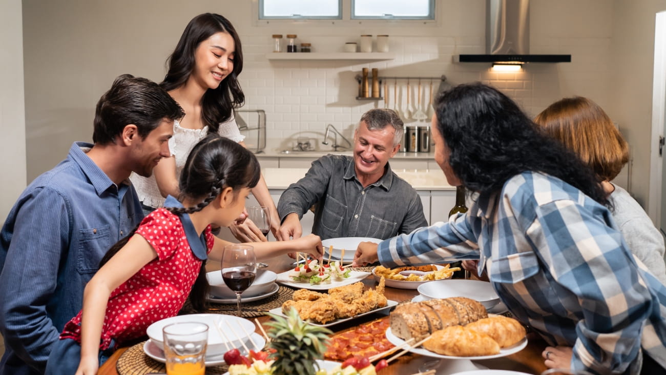 Multi-ethnic big family having dinner, enjoy evening party in house. Attractive group of diverse people having fun, eating foods, celebrate weekend reunion gathered together at dining table at home.