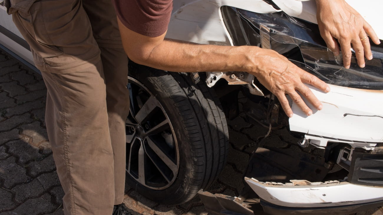 Man checking out the damage to the right front end of his car that was in a collision