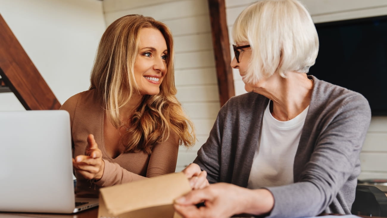Portrait of woman talking with retired mother at home in front of laptop.