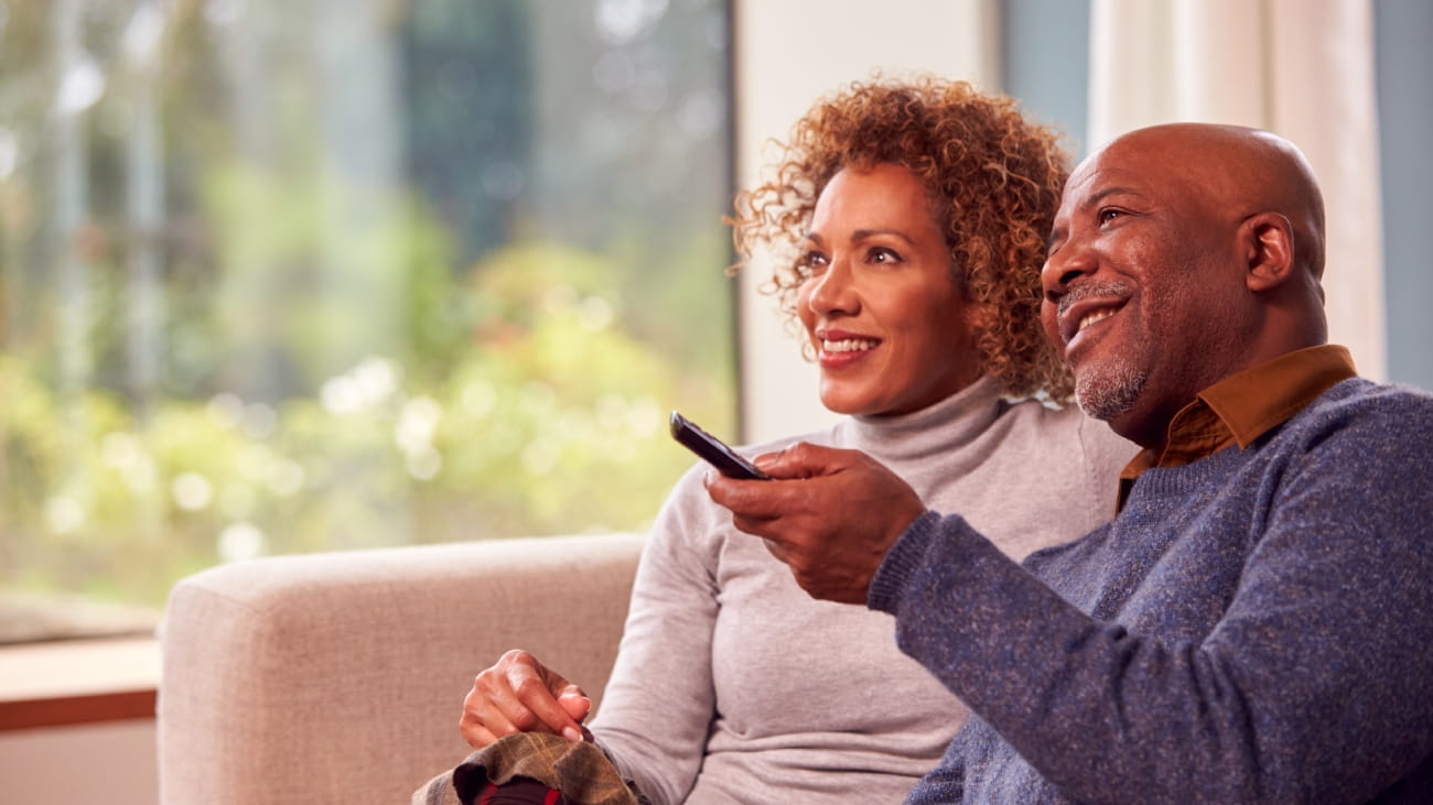 Senior Couple Sitting On Sofa At Home Watching TV Together