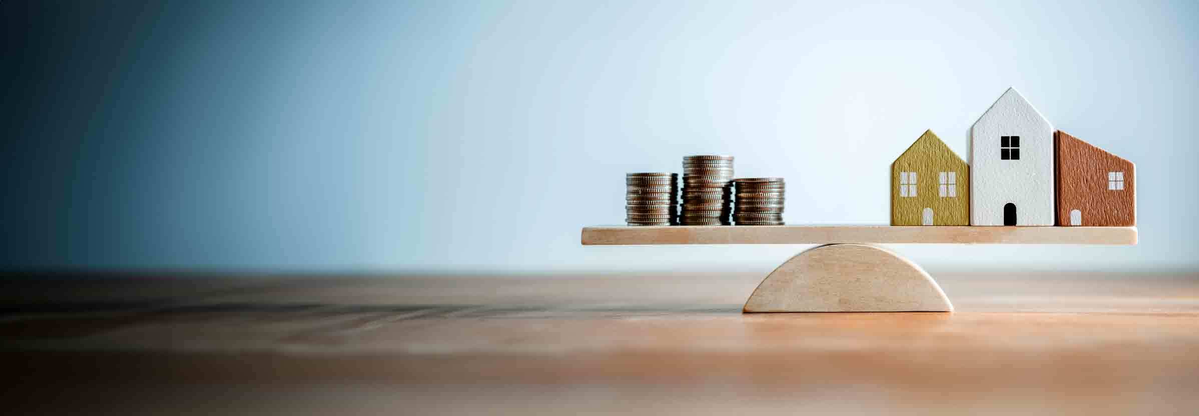 small wooden houses and 3 piles of coins on opposite ends of a seesaw