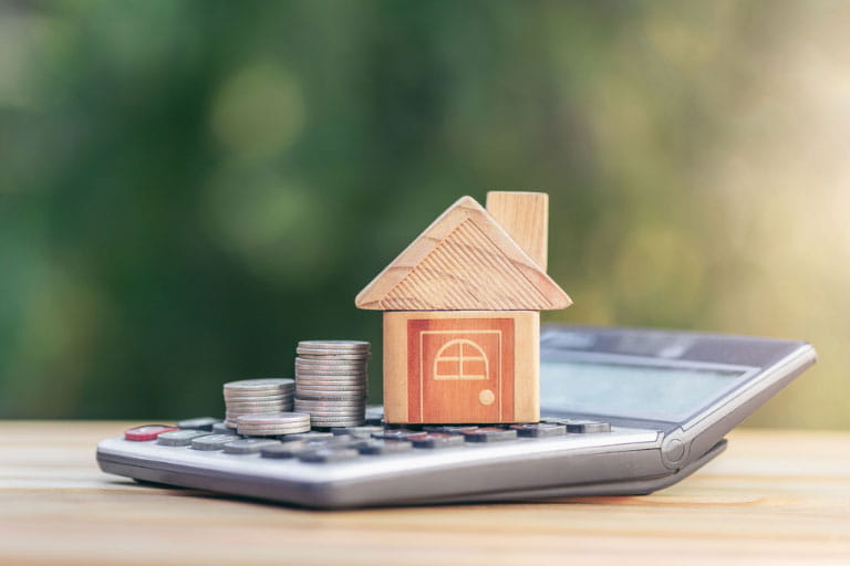 Model house on a calculator next to a stack of coins