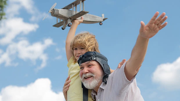 A grandfather carrying his grandson in the air as they play with a toy airplane