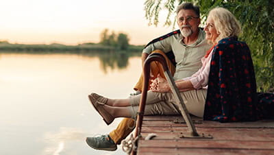 Mature couple relaxing on a pier, sharing a blanket and enjoying the sunset over the lake.