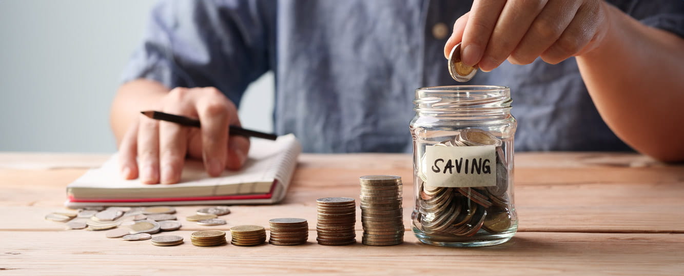 A table with piles of coins in increasing heights with a glass jar full of coins next to them with a label saying savings