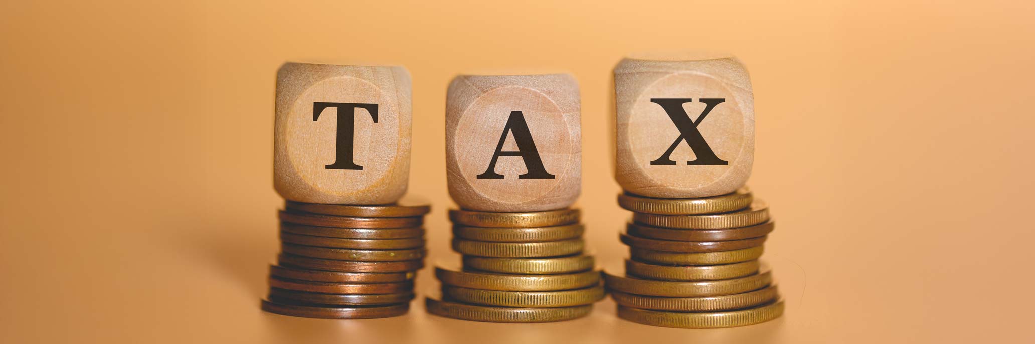 The word tax written on wooden dice lying on top of stacks of coins in a studio shot.